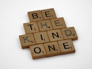 Scrabble tiles arranged to spell 'BE THE KIND ONE' on a white background, emphasizing kindness.